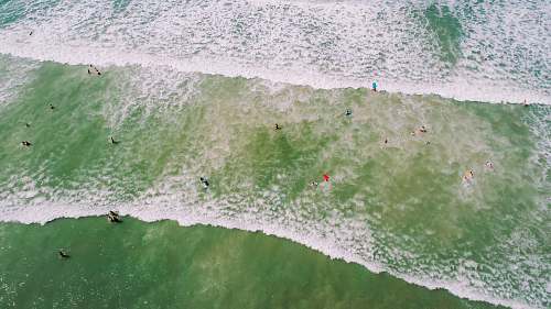 cocoa beach aerial photo of people on seashore with waves and bubbles at daytime drone view